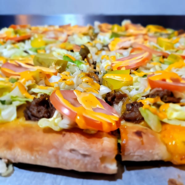 Close-up of a Pronto Pizzeria pizza topped with lettuce, tomatoes, ground beef, and cheese sauce.