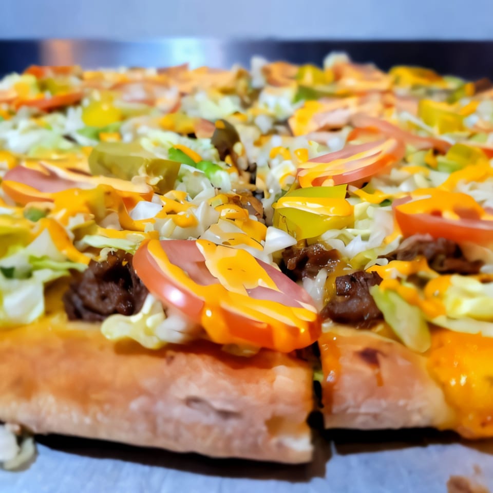 Close-up of a Pronto Pizzeria pizza topped with lettuce, tomatoes, ground beef, and cheese sauce.