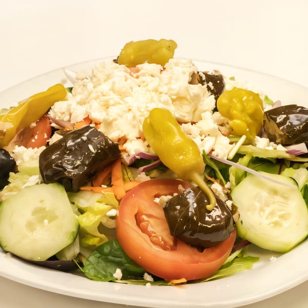 A close-up of a Pronto Pizzeria salad with feta, pepperoncini, stuffed grape leaves, tomatoes, and cucumbers.