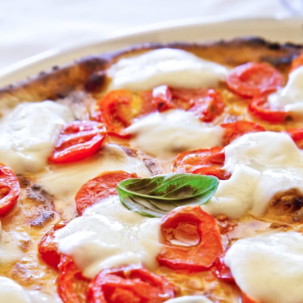 Close-up of a Pronto Pizzeria pizza with melted mozzarella, sliced tomatoes, and a basil leaf.